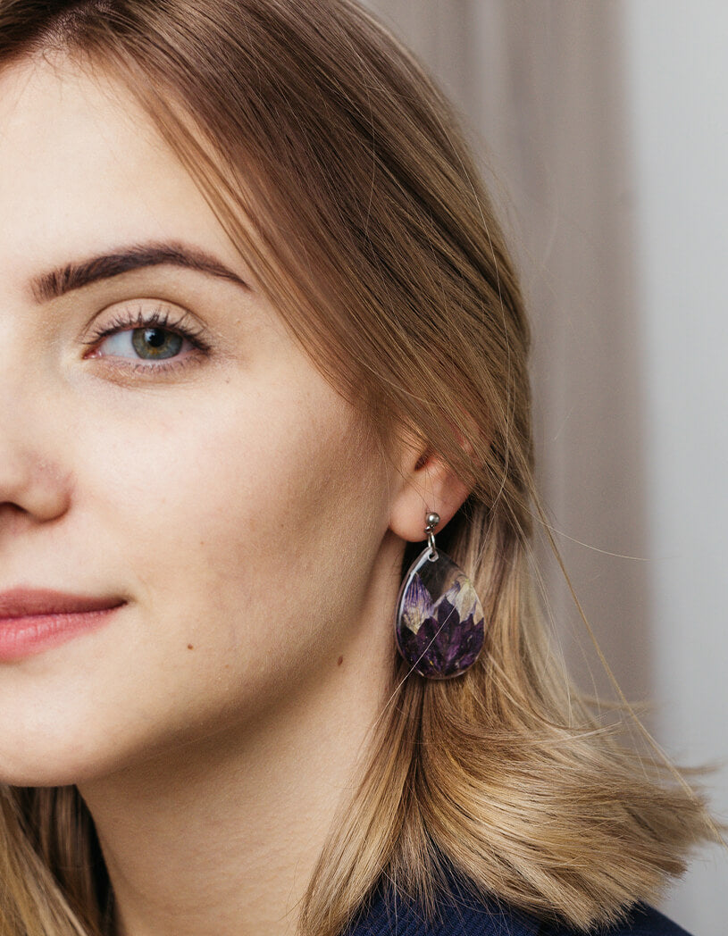 Close-up of a woman wearing a purple feather earring with a neutral background and thin, arched brows