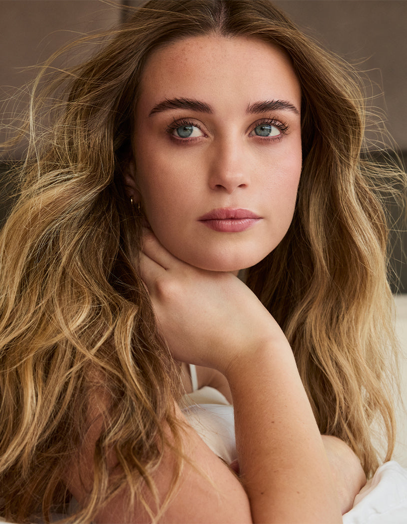 Woman with long, wavy hair posing with a neutral background
